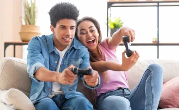 Two teens excitedly play video games on a couch.