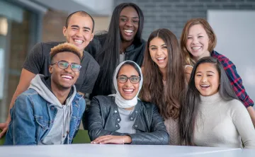 A diverse group of post-secondary students smile around a table.