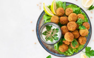 A blue bowl of falafels on a bed of lettuce with a side sauce.