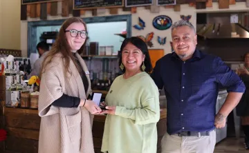 Group of three people standing together, one woman is presenting a medal to another. 